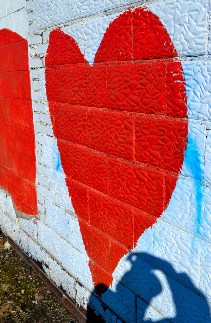 a person is casting a shadow on a red painted heart on a brick wall