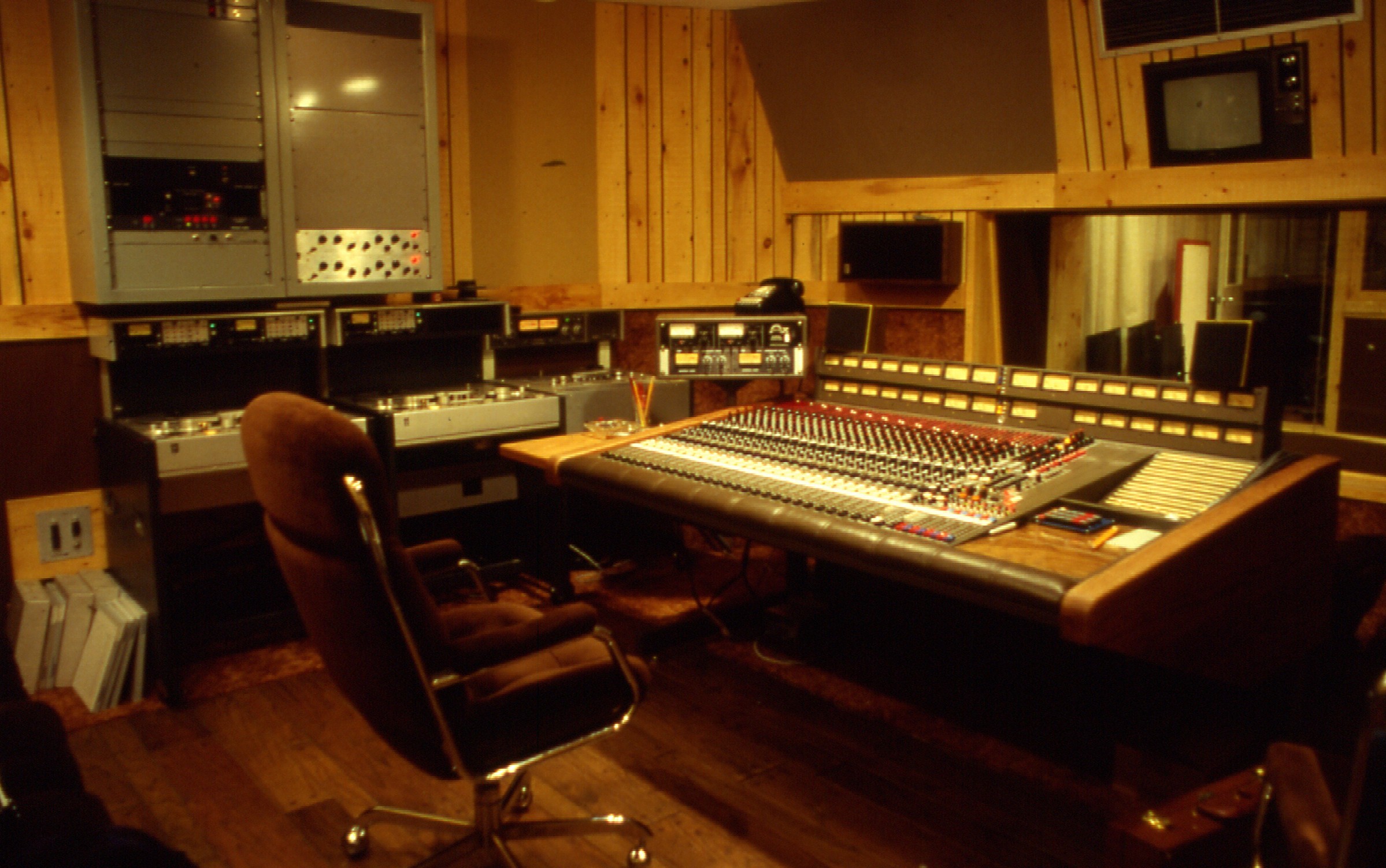 a room with wooden walls, a mixing board, a chair and several computers