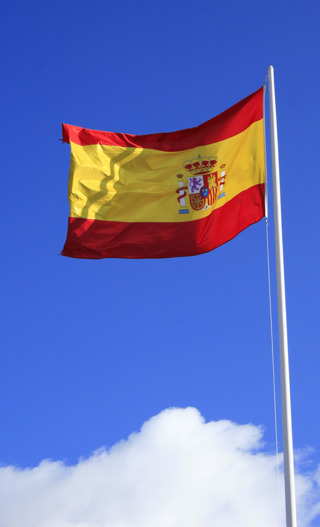 the spanish flag flies on a flagpole with clouds in the background
