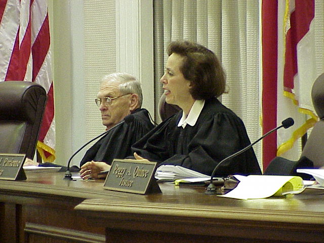 the judge and judge are seated side by side in front of an american flag
