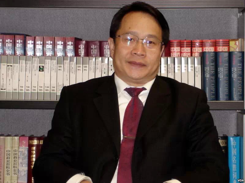 an asian man in a suit sitting in front of a bookshelf