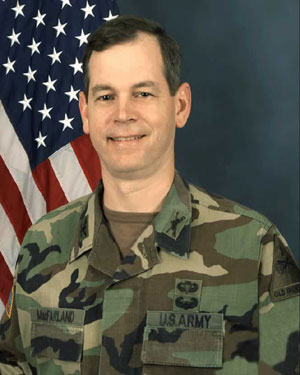 a man in a camouflage uniform stands in front of a flag
