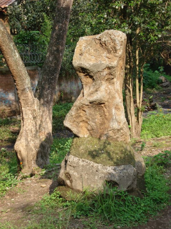 large rock with a smaller rock sticking out of the center, next to some trees