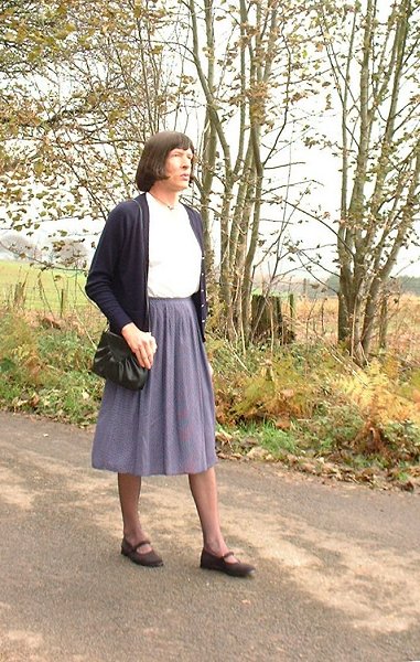 a woman is standing by a tree on the side of the road