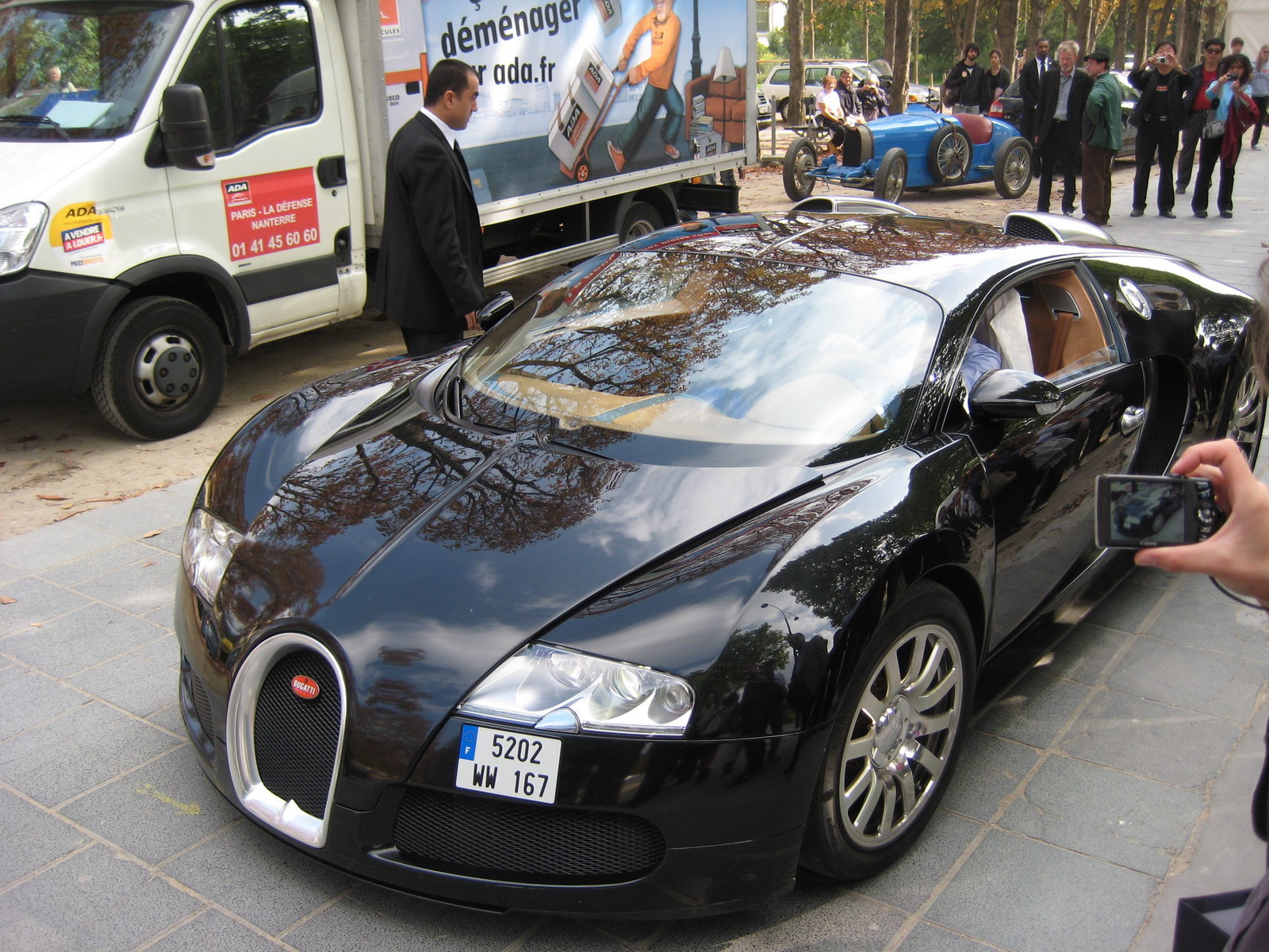 a black bugatti car parked in front of a bus