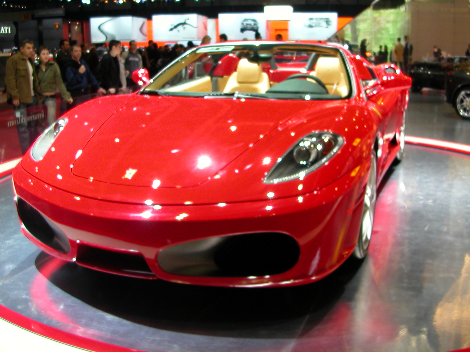 a red car on display at a showroom with people looking