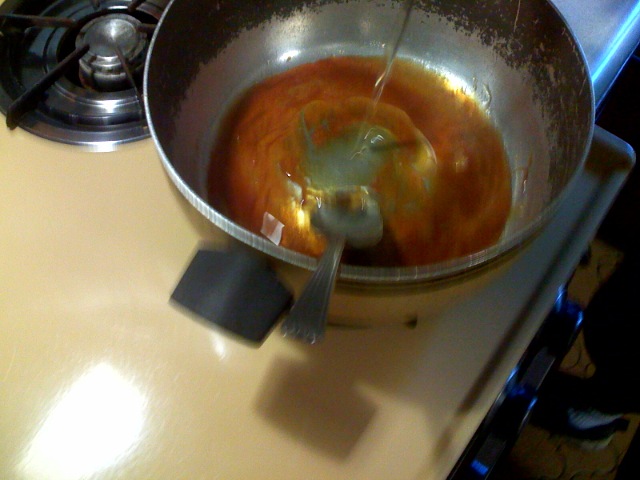 a metal bowl containing orange sauce cooking on the stove