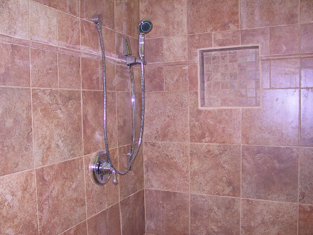 a tan tiled shower is shown with a hand shower
