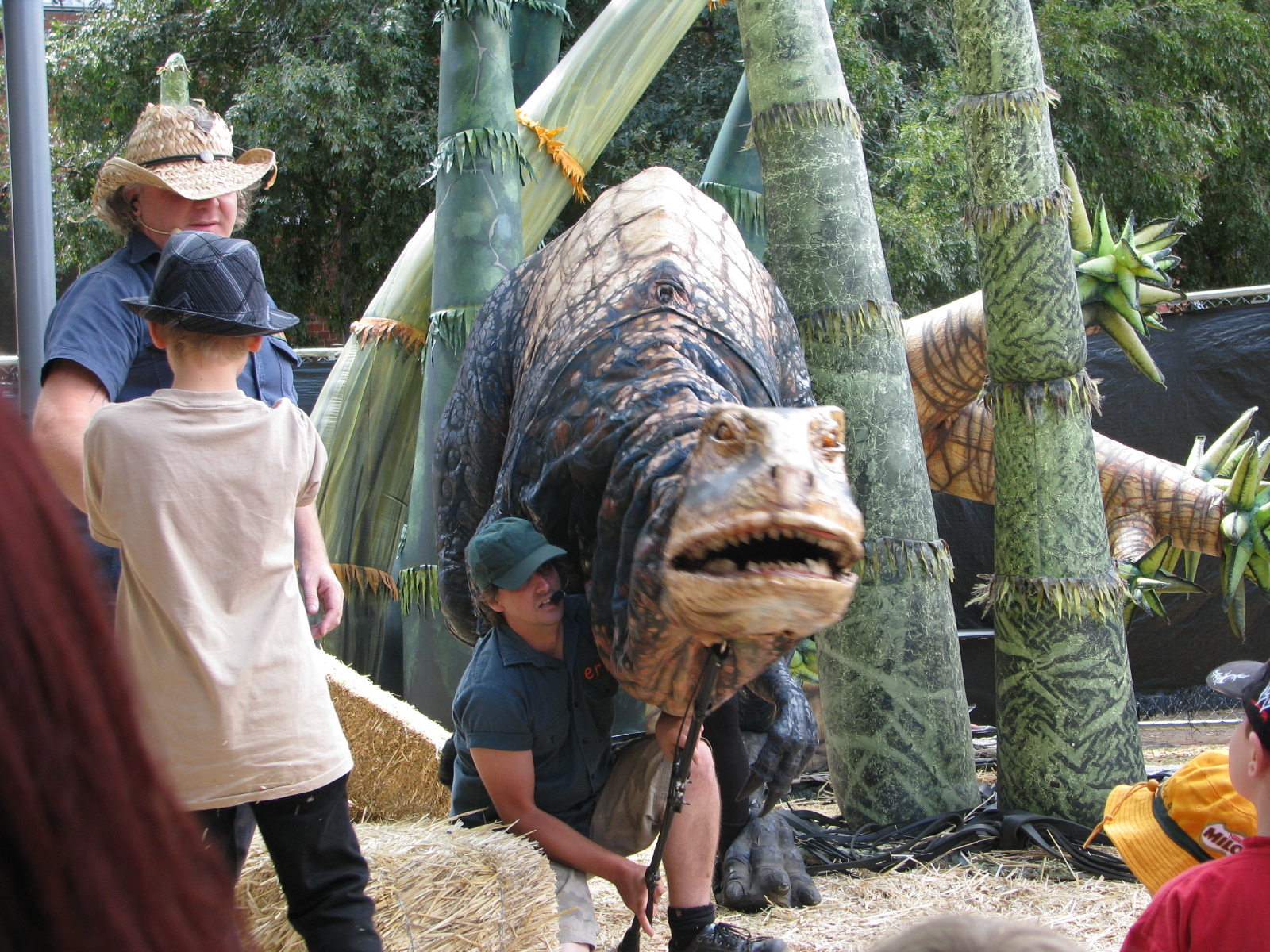 children looking at a dinosaur statue with a man in a straw hat
