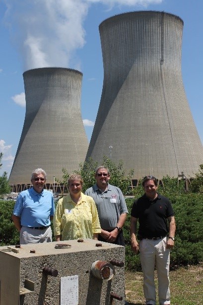 two large cooling towers behind three men