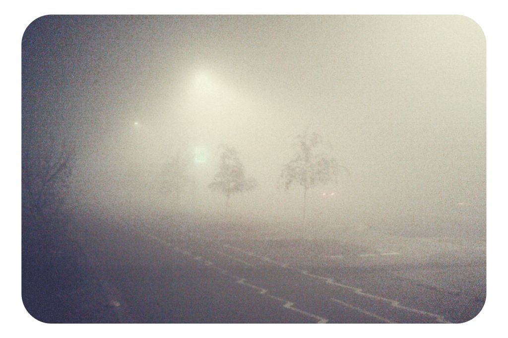 a foggy street with no cars and a person walking down the road