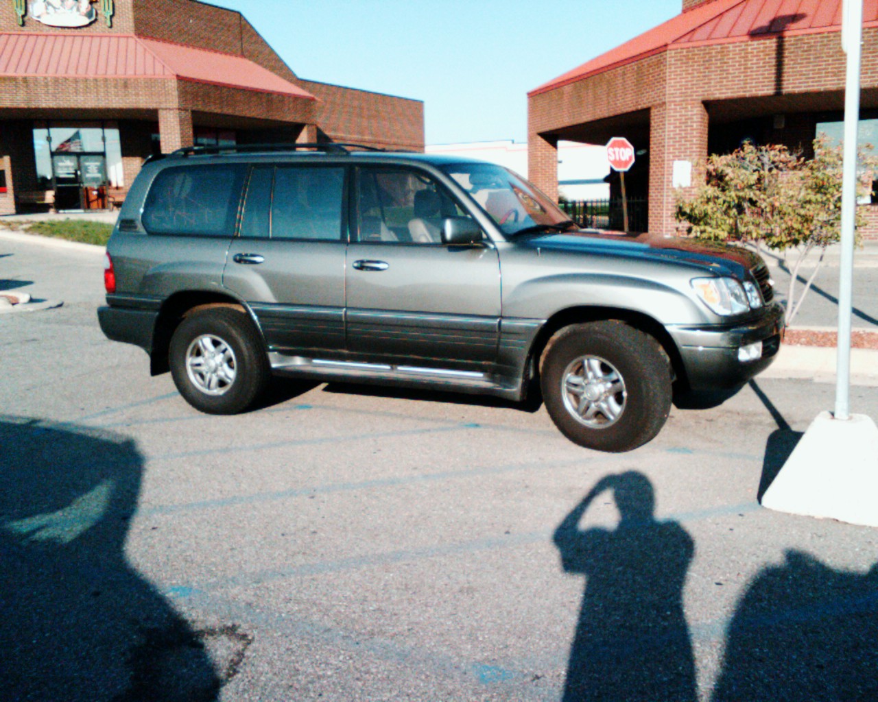 the shadow of a person with the car behind him on a parking lot