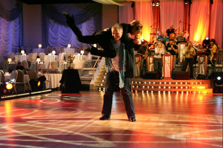 two people dance on an indoor dance floor while spectators watch