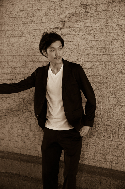 an asian man posing next to a brick wall