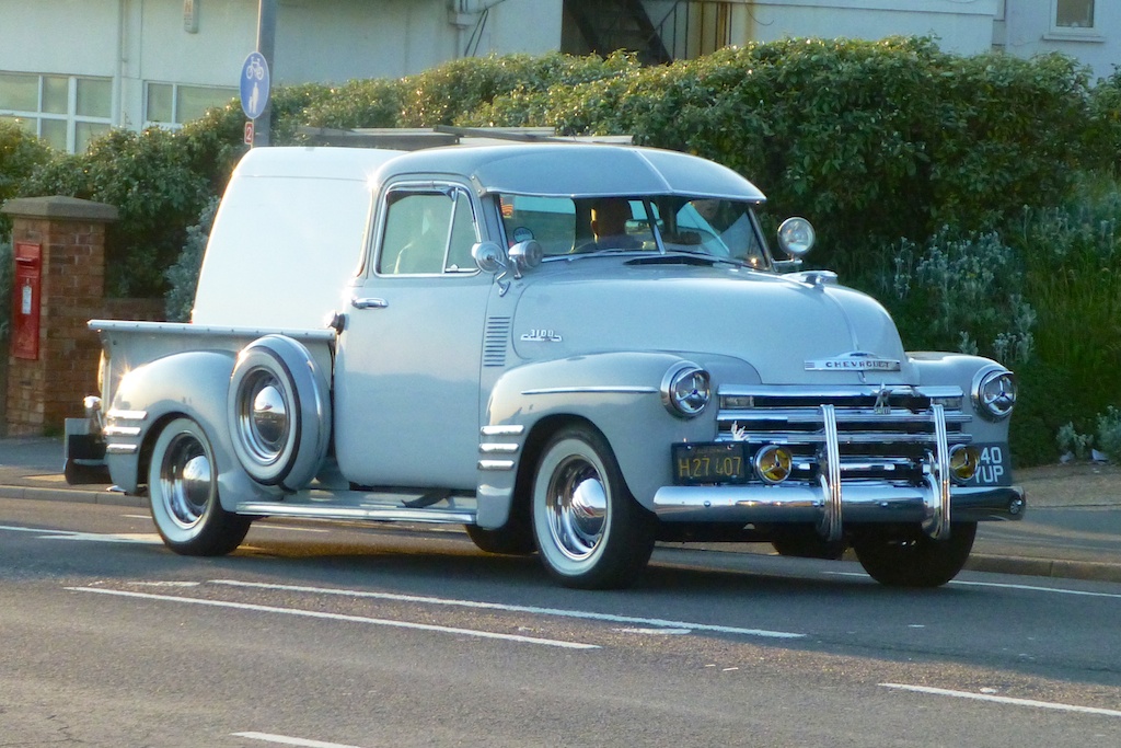 an old truck driving on the street next to a hedge