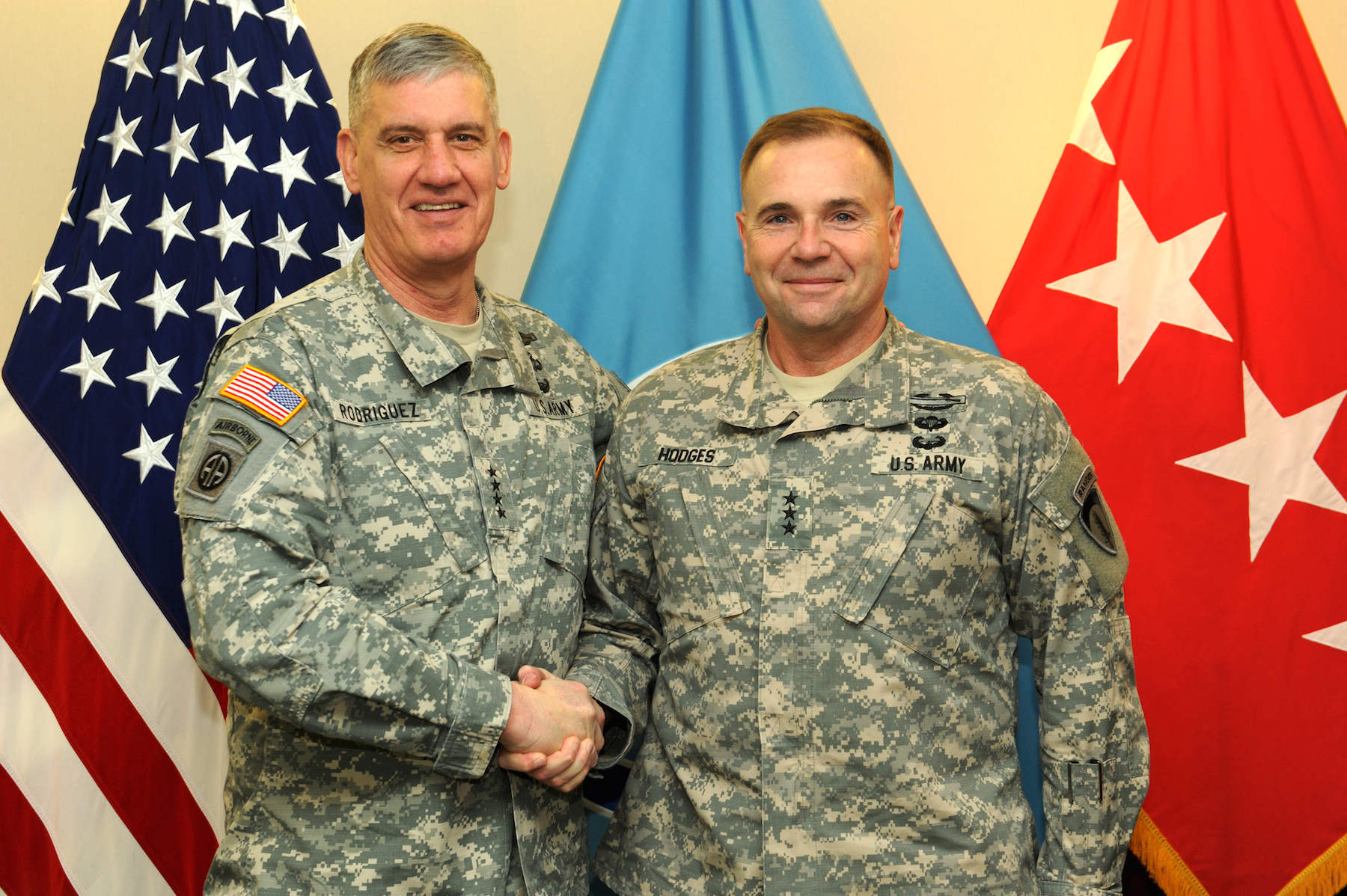 two military men shaking hands with flags in the background
