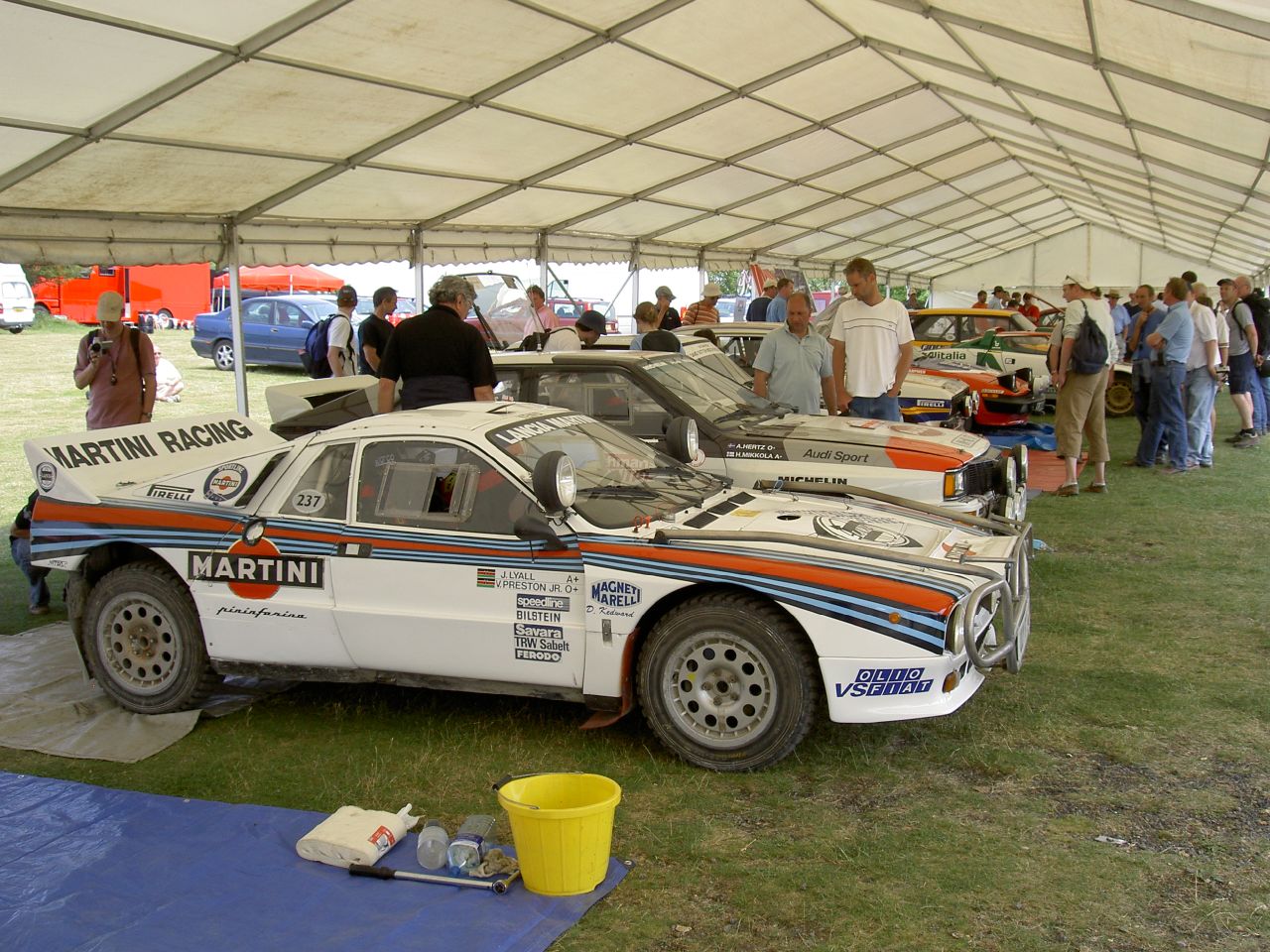 a car is parked under a large tent and people are standing around