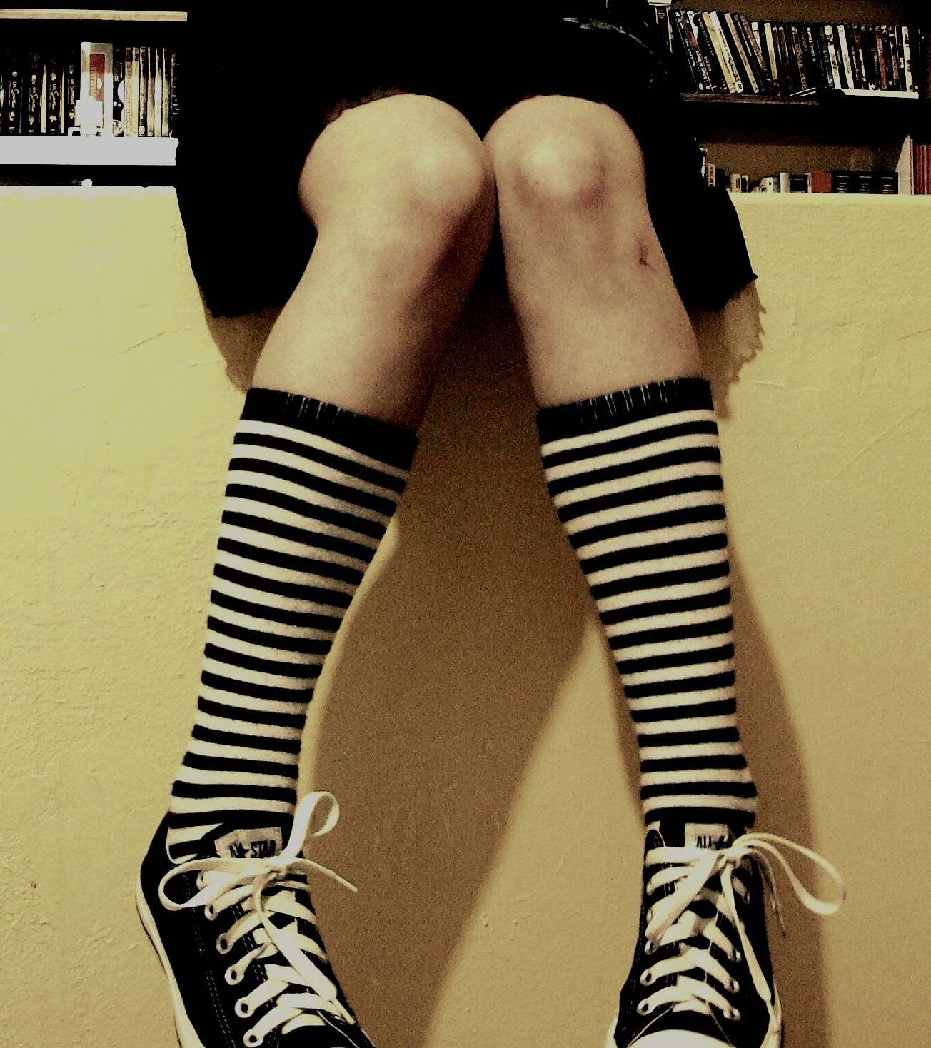a girl wearing a black and white striped sock on a shelf with a bookcase behind her