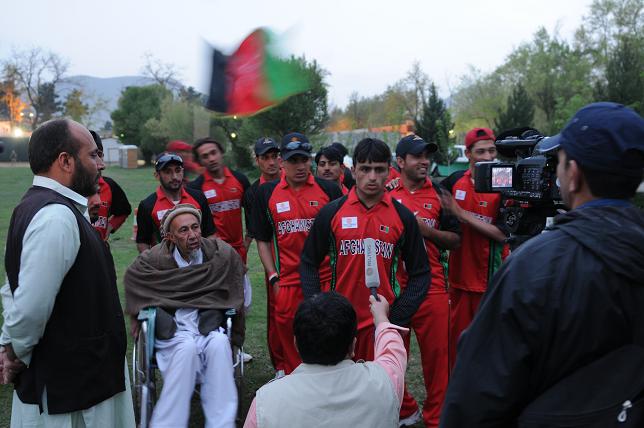 group of men and one person in a red uniform on a field with a flag