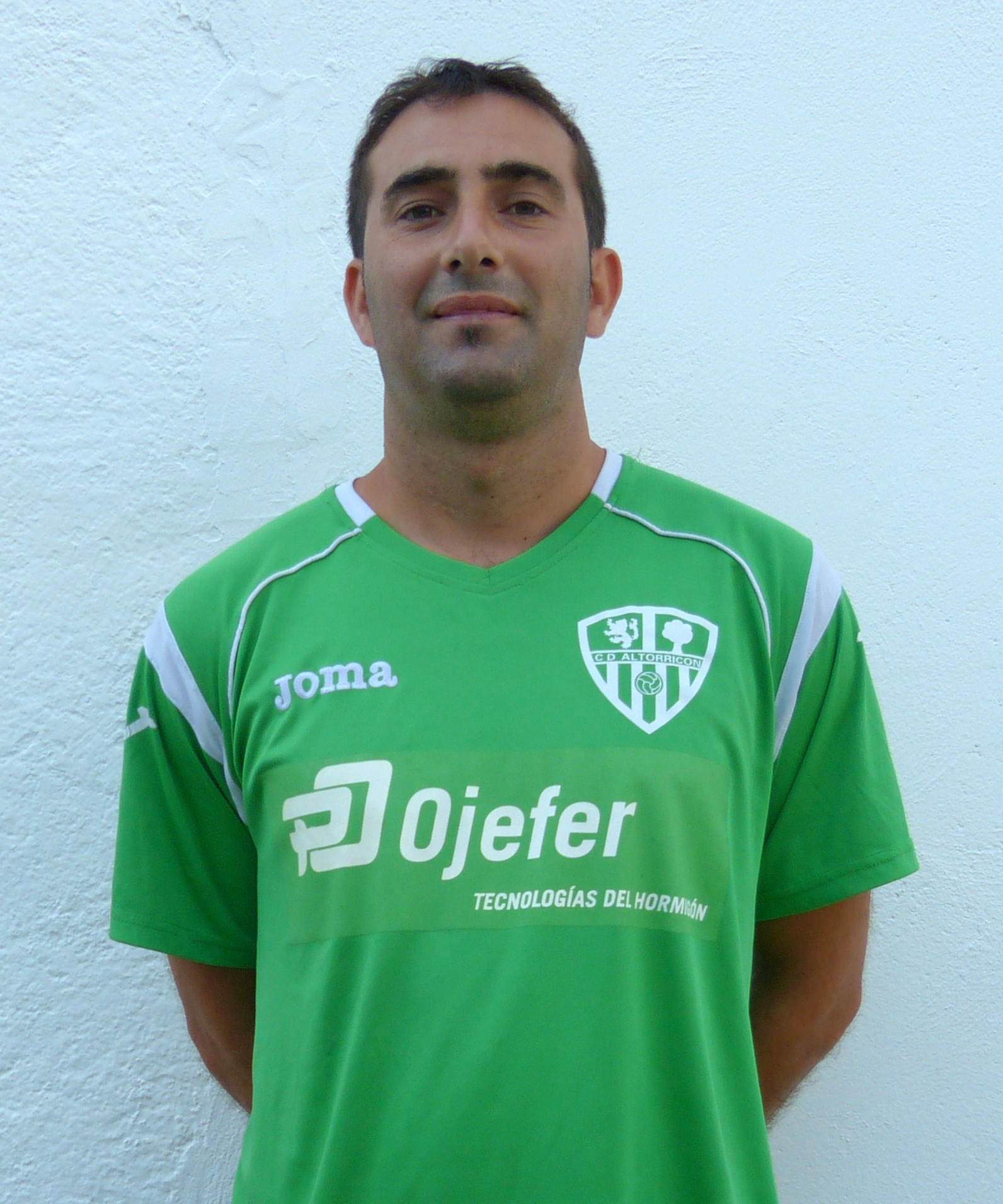 a man in a green jersey standing near a white wall