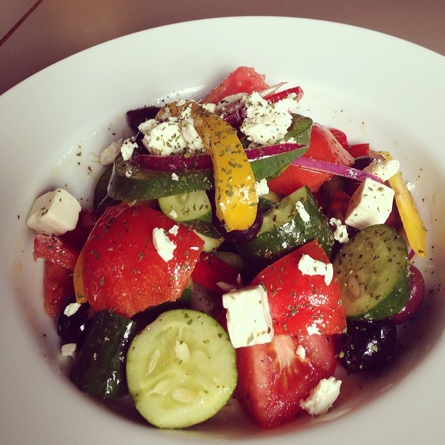 the plate holds a salad with cucumbers, tomatoes and other vegetables