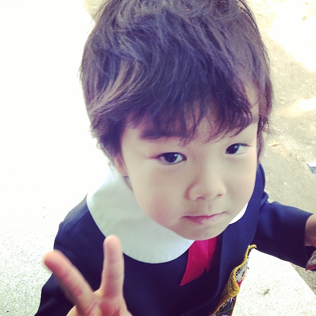 an asian toddler girl wearing a school uniform and giving the peace sign