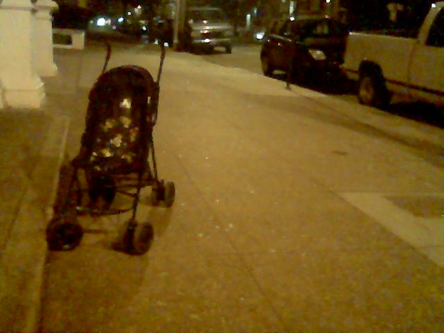 a stroller with wheels on the sidewalk near a curb