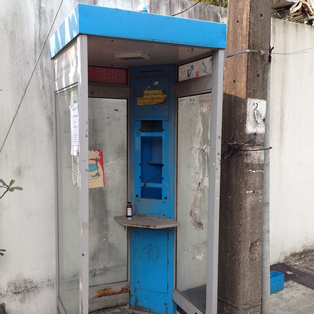 an old, broken blue portable telephone booth next to a street