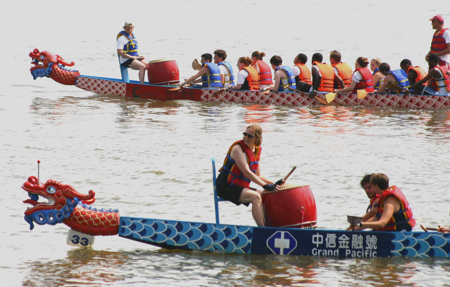 a dragon boat with two women on the front and men in the back paddling behind it