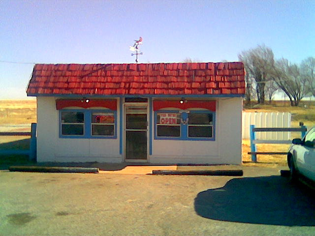 an old style store with a red roof sitting in front of a green car