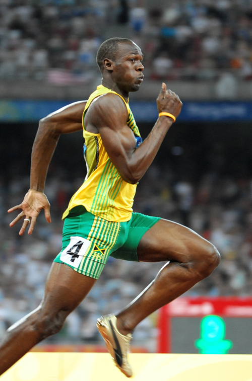 a man in green shorts and a yellow top running on the track