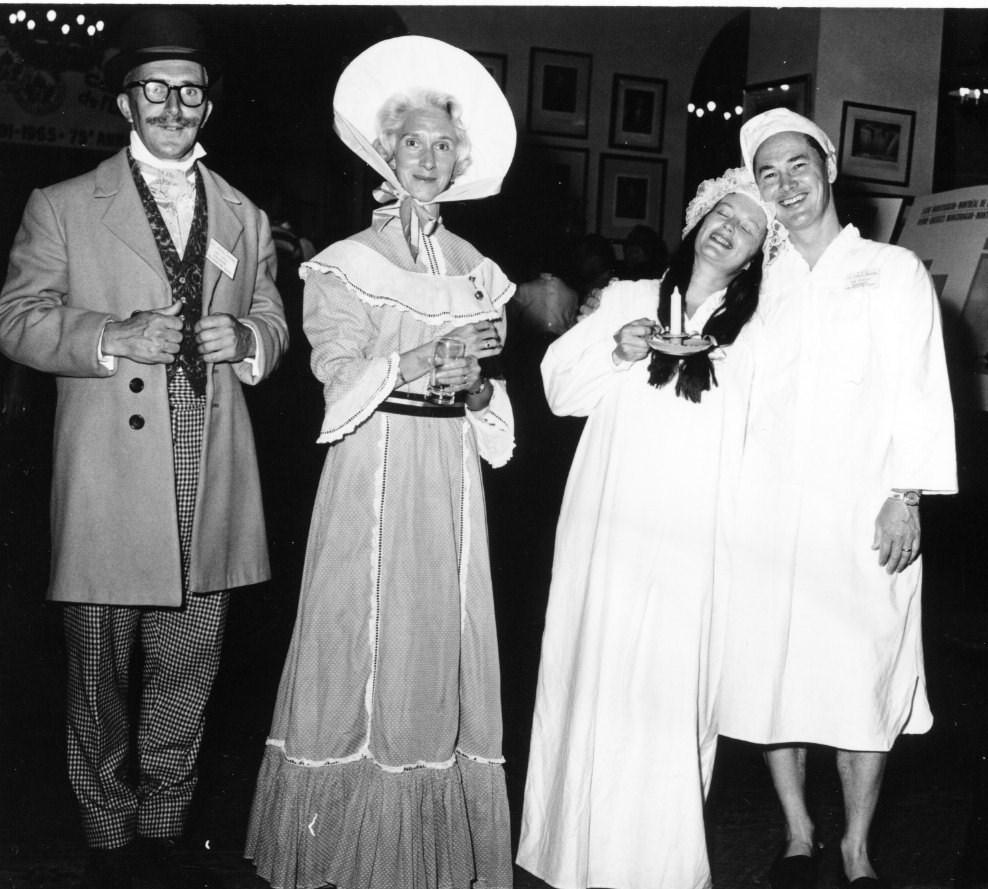 three women in dresses and hats posing with a man in a suit