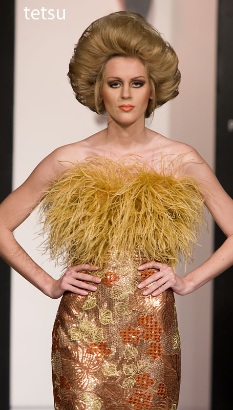 a woman walks down a runway wearing a golden feathered dress