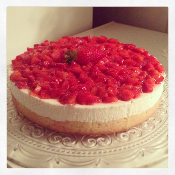 a cheesecake with strawberries on top sits on a glass plate