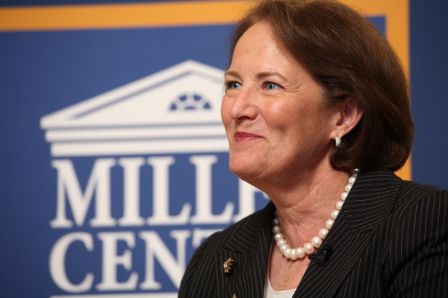 a woman in a suit and pearls stares towards the camera