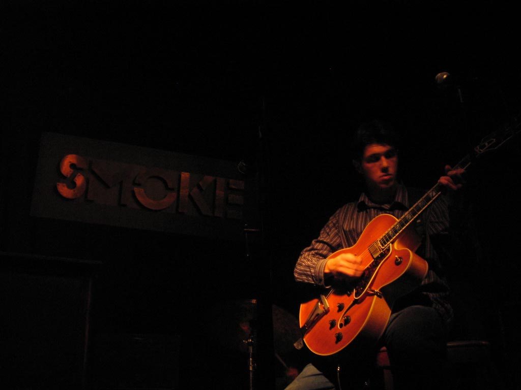 a man sitting in a dark room holding a guitar