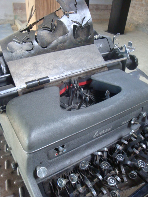 an old typewriter with paper and several other pieces of equipment