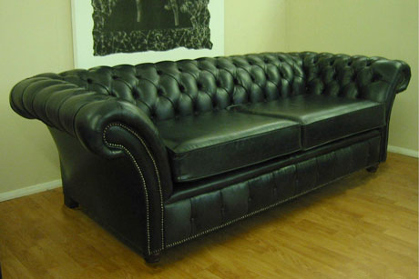 an old black leather couch in an empty living room