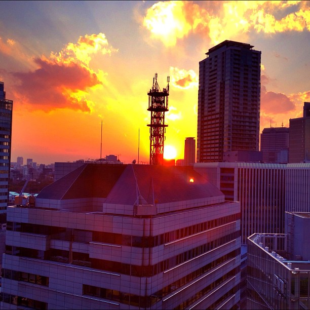 the sun is setting on the city and behind some tall buildings