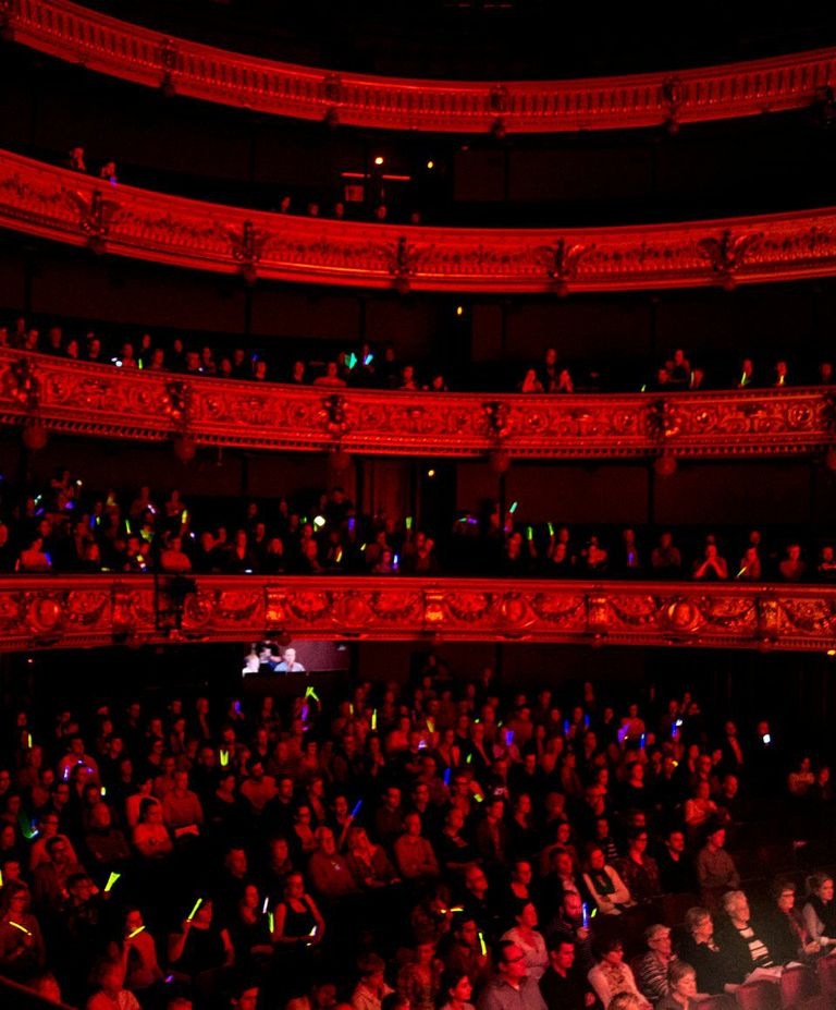 a group of people in an auditorium with red light from the stage