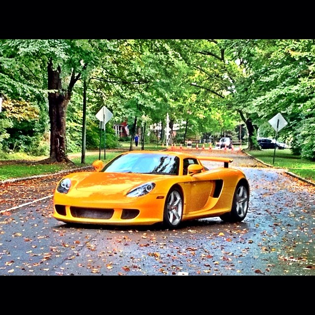 a yellow sport car driving down the street with some trees on either side