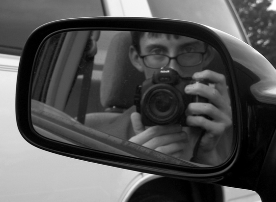 a man with glasses taking a picture in a car mirror