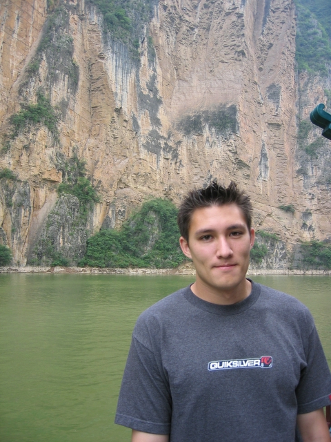 a young man standing on a river next to a tall mountain