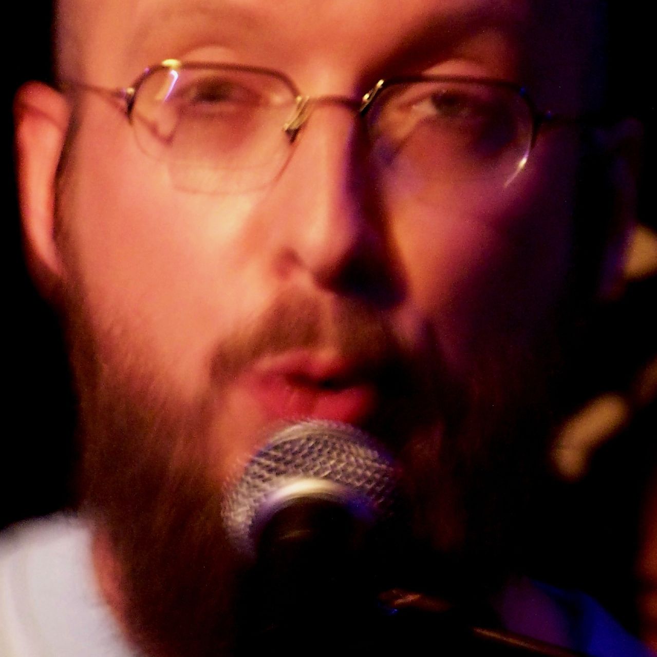 man with beard and glasses holding up a microphone