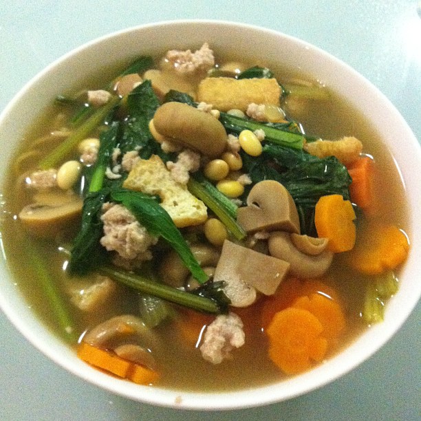 a white bowl of soup with carrots, spinach and other foods