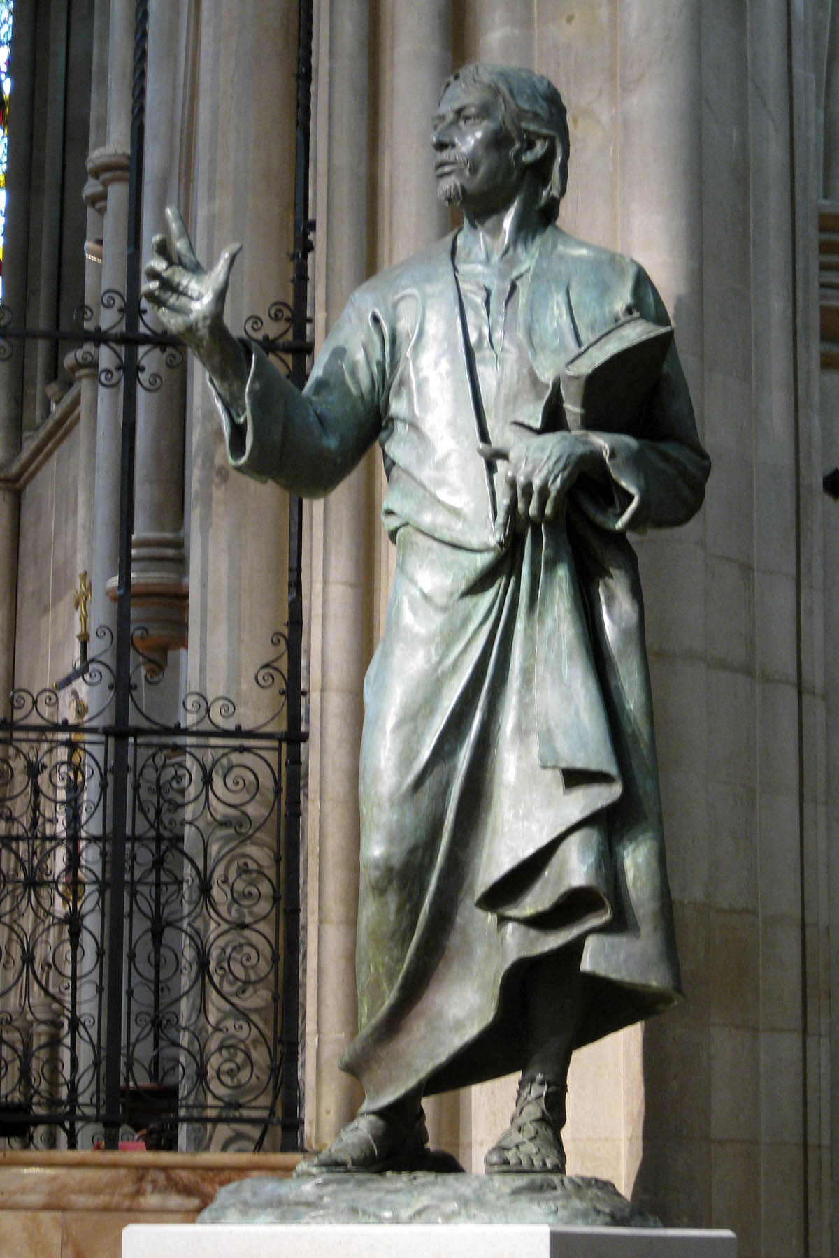 statue of a person with a book in his hand in front of a church
