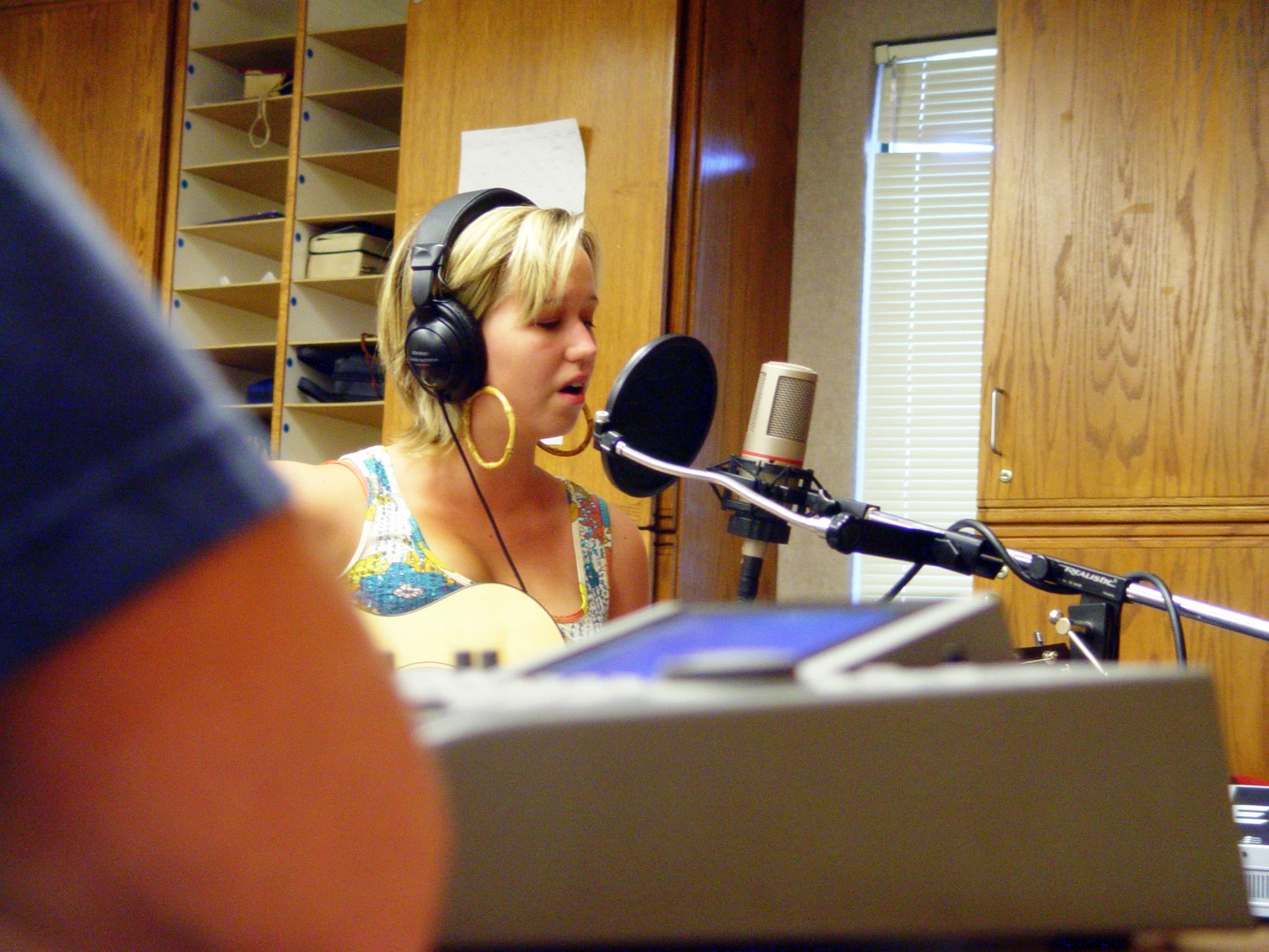 a woman sitting in front of a microphone in front of a recording booth