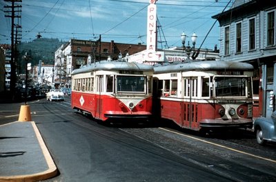two public transit trains on a street in the past