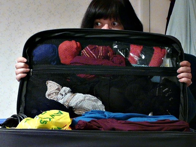 woman sitting in open suitcase of clothing with hand on chest