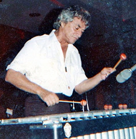 an older man in white shirt holding a drum